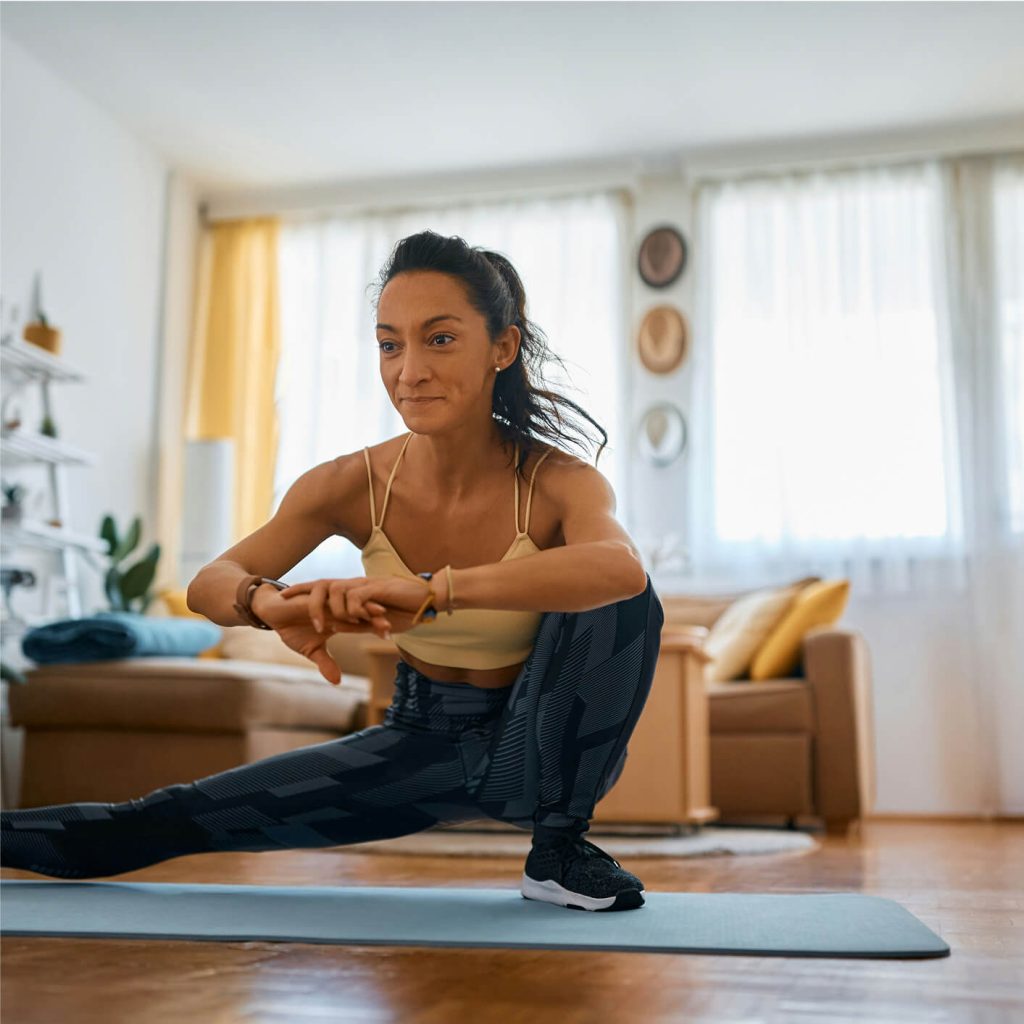 A woman in athletic wear performs a side lunge stretch on a path outdoors.