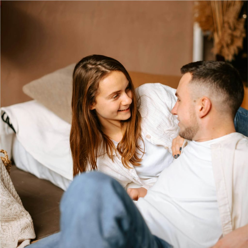 A woman and man are sitting close together on a bed or couch.