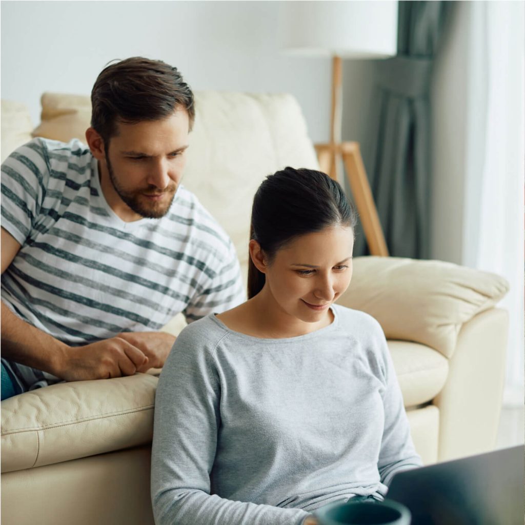 A man and a woman sit indoors, looking at a laptop together.