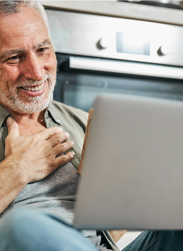 Older man with gray hair and beard smiling, holding his chest.